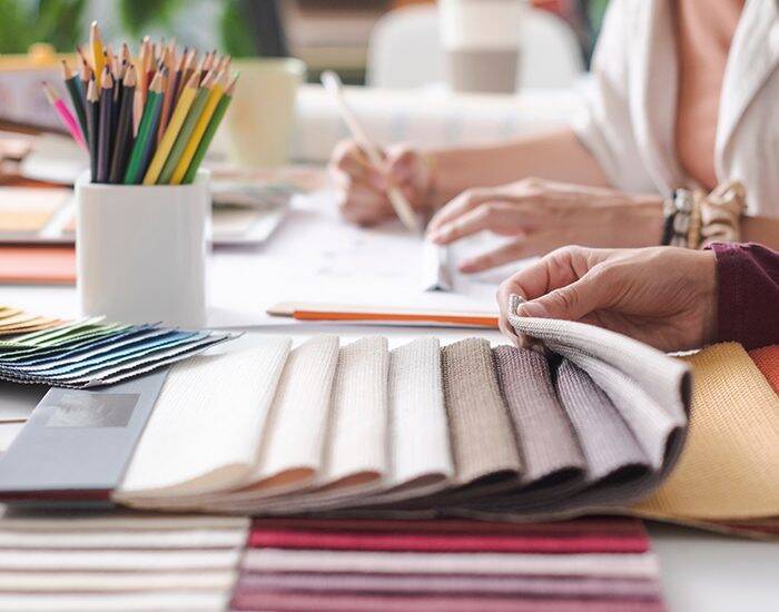 Interior Designers are comparing fabric swatches. A white vase contains many colorful pencils.