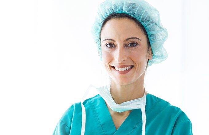 Woman in healthcare setting wearing a cap, scrubs, and mask.